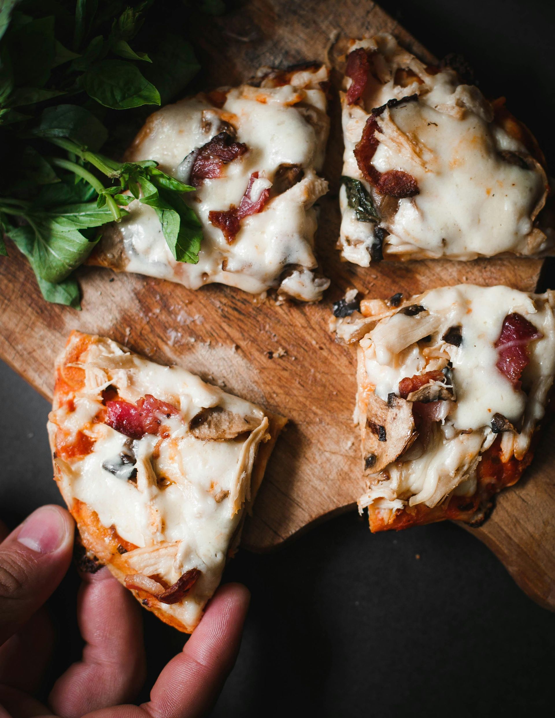 A person is holding a slice of pizza on a wooden cutting board.