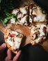 A person is holding a slice of pizza on a wooden cutting board.