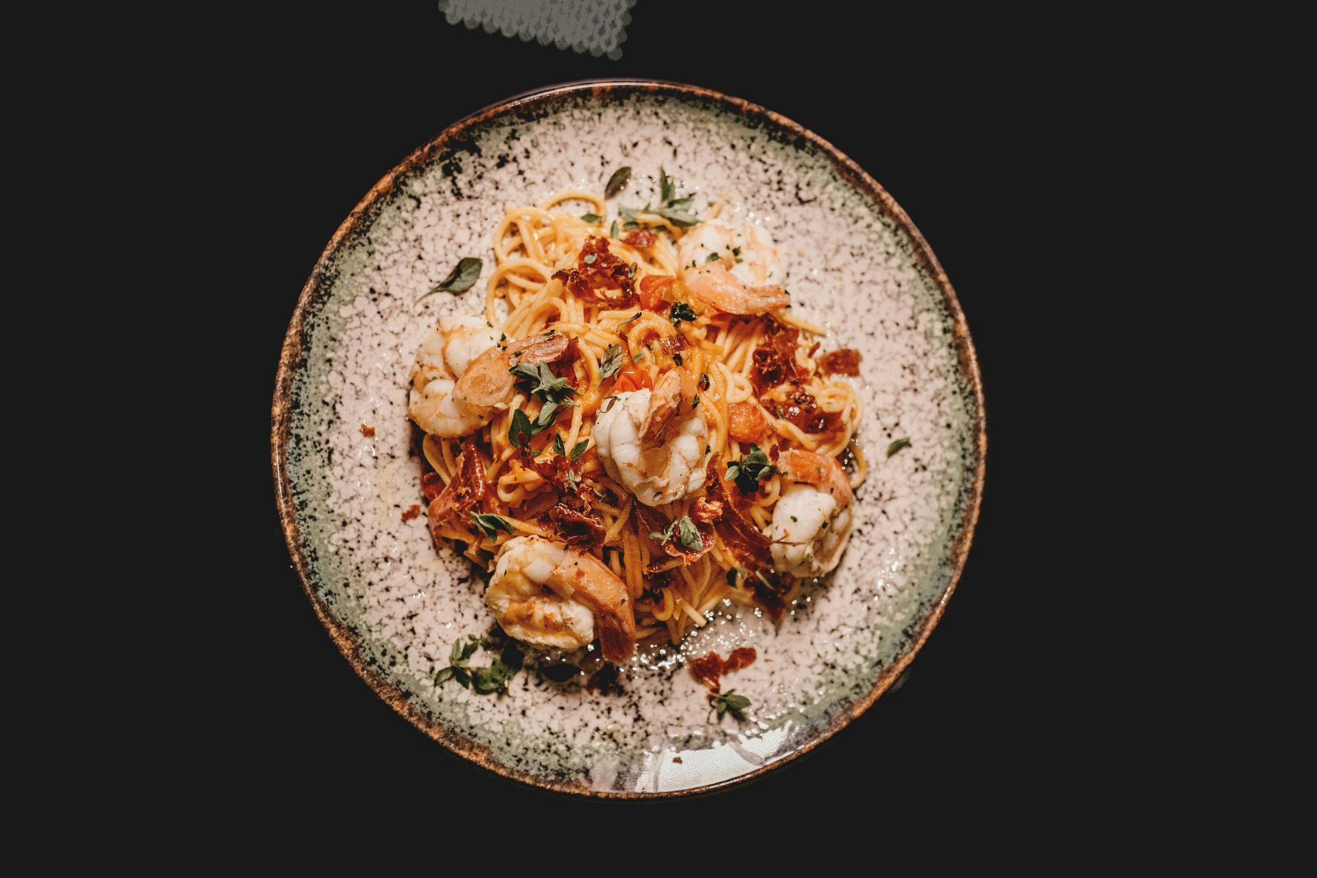 A plate of pasta with shrimp and bacon on a black background.
