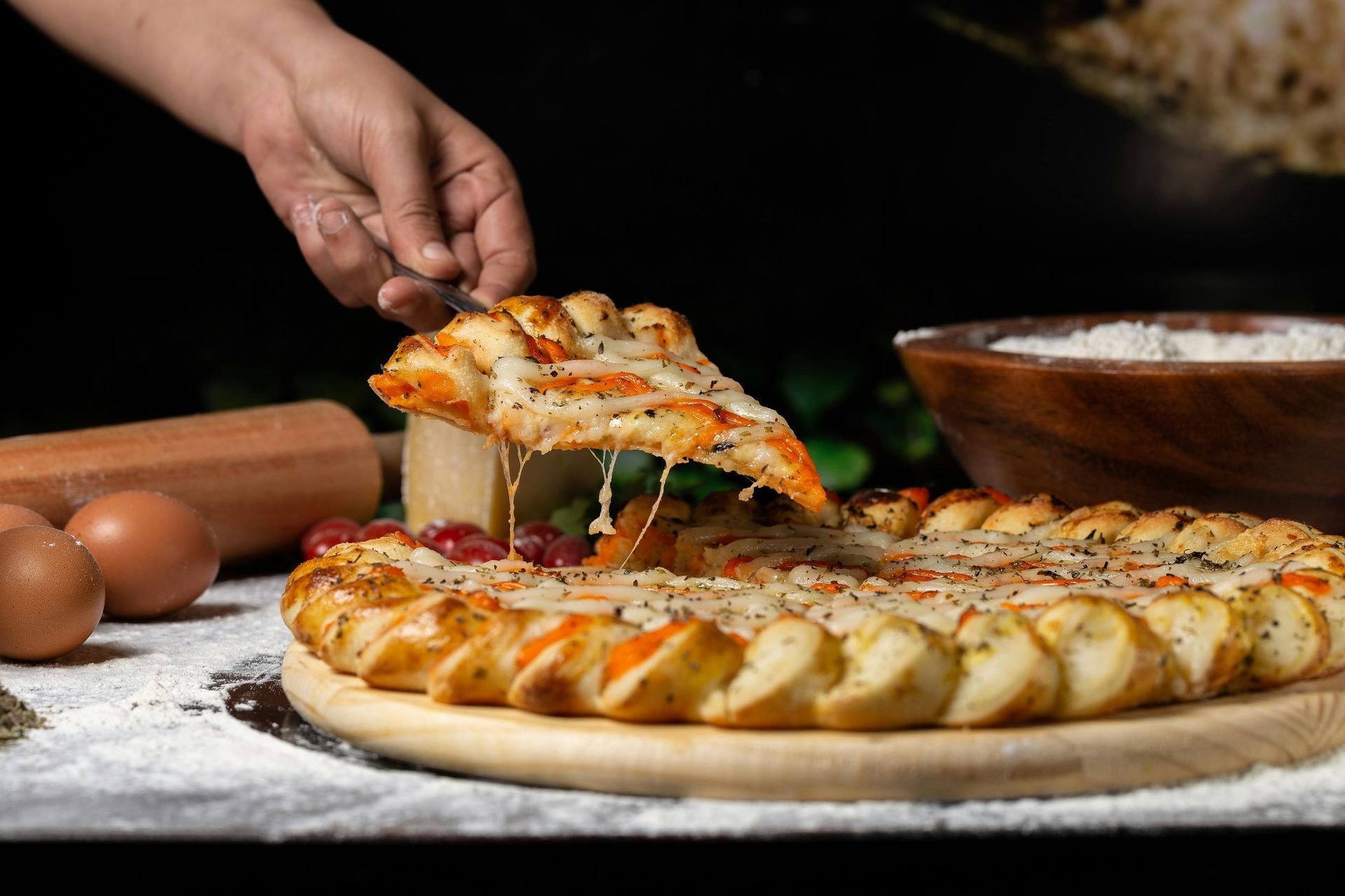 A person is taking a slice of pizza from a pizza on a wooden cutting board.