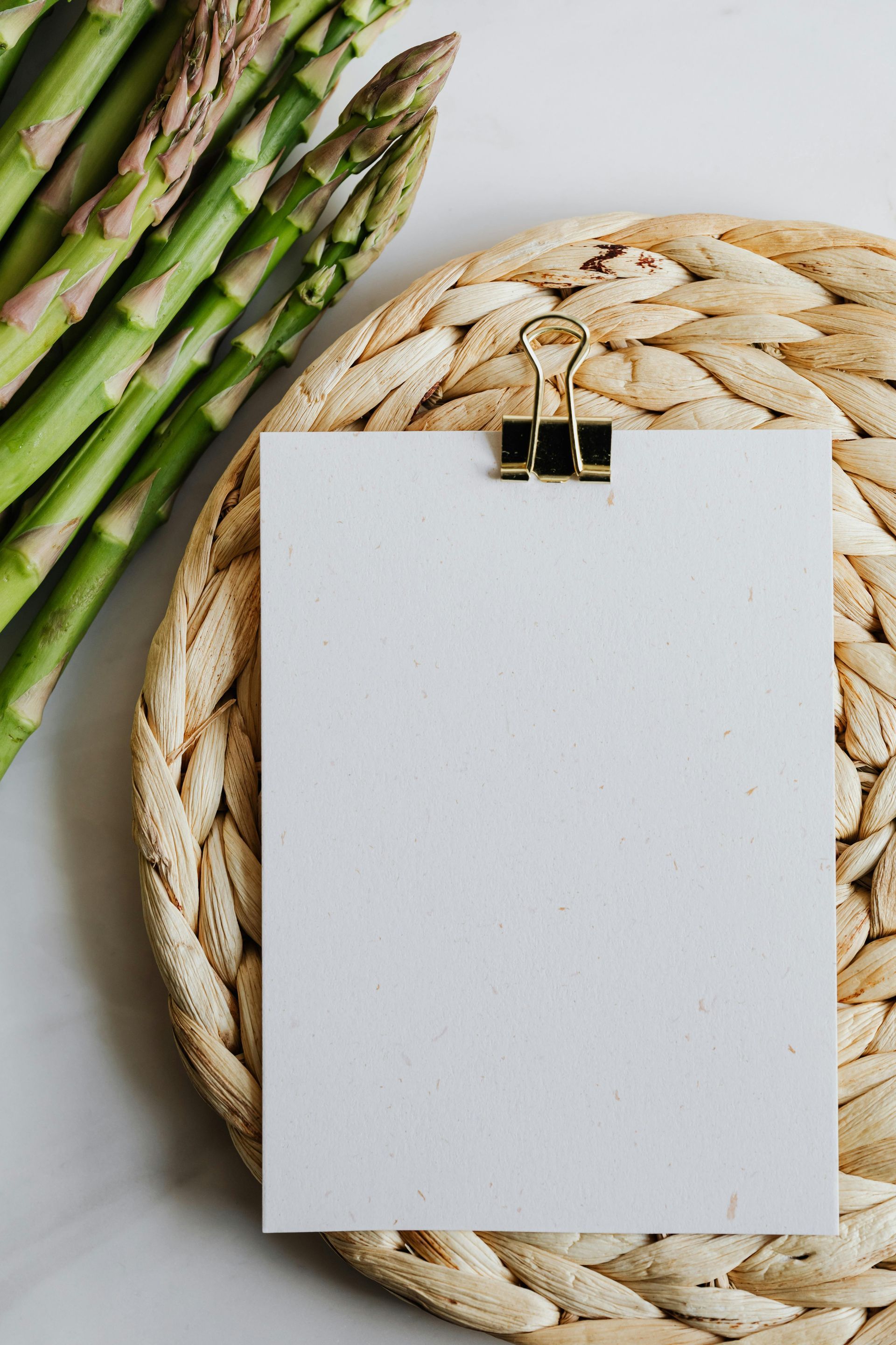 A piece of paper is sitting on a wicker place mat next to asparagus.