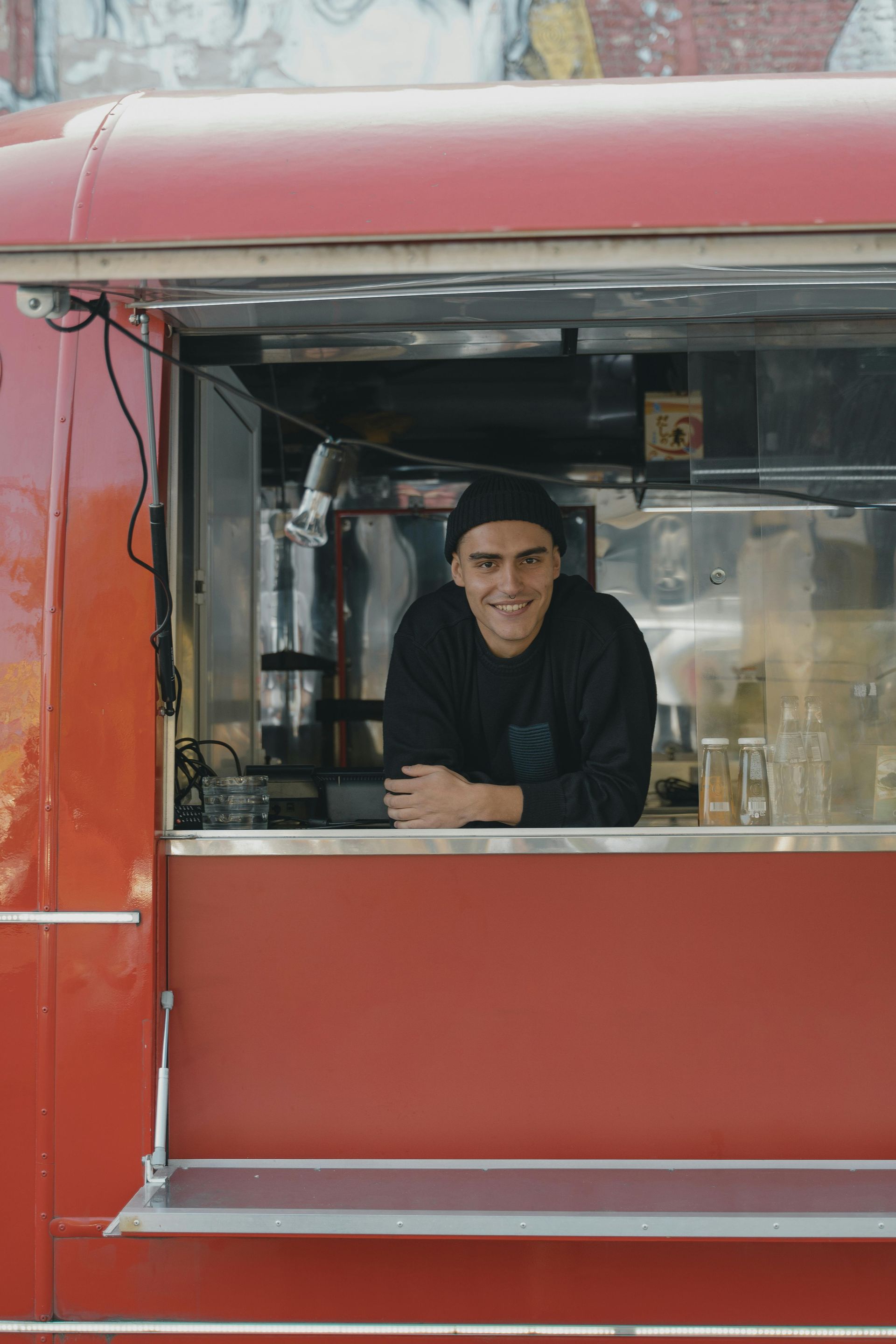 A man is standing in a red food truck looking out the window.