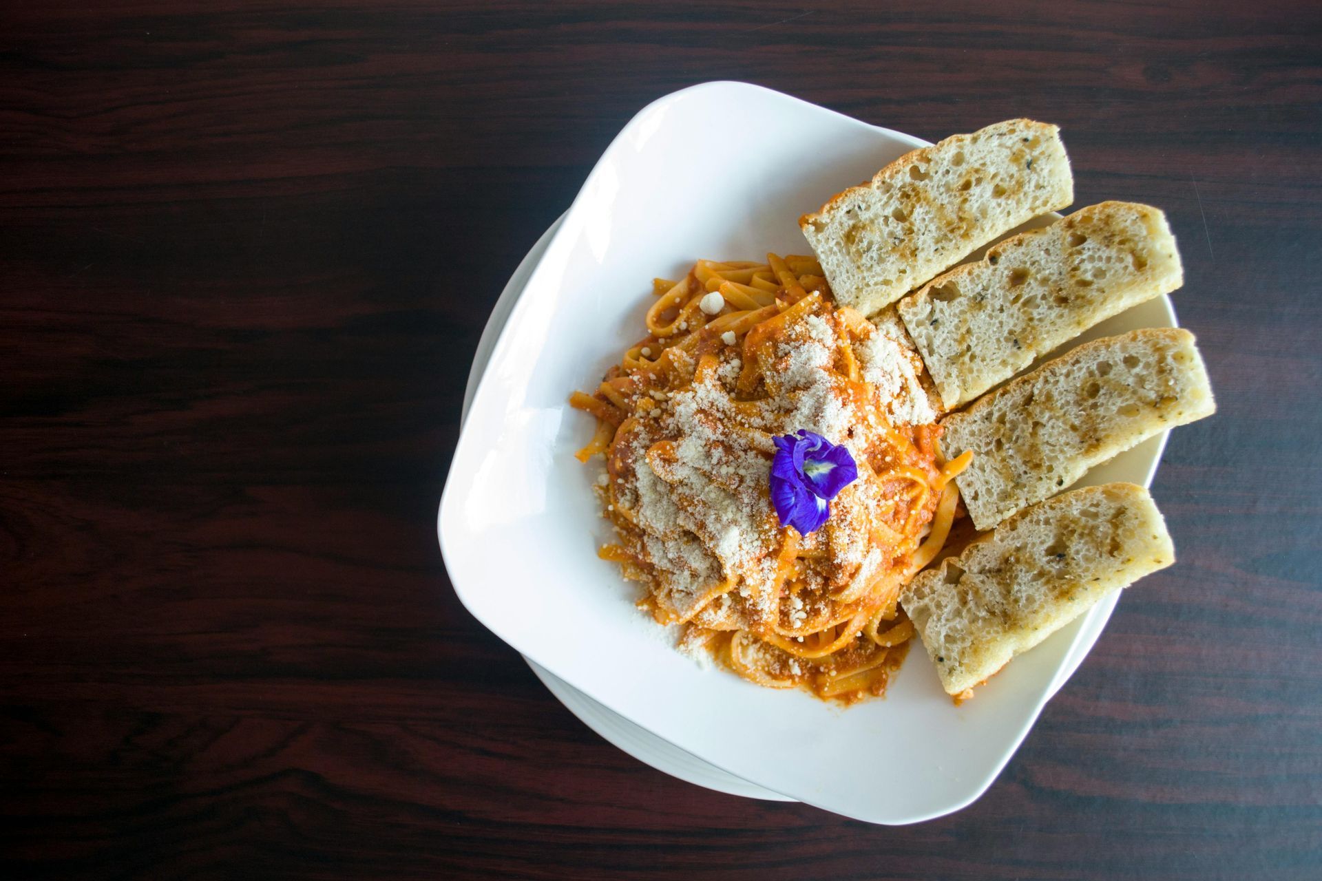 A white plate topped with spaghetti and garlic bread on a wooden table.
