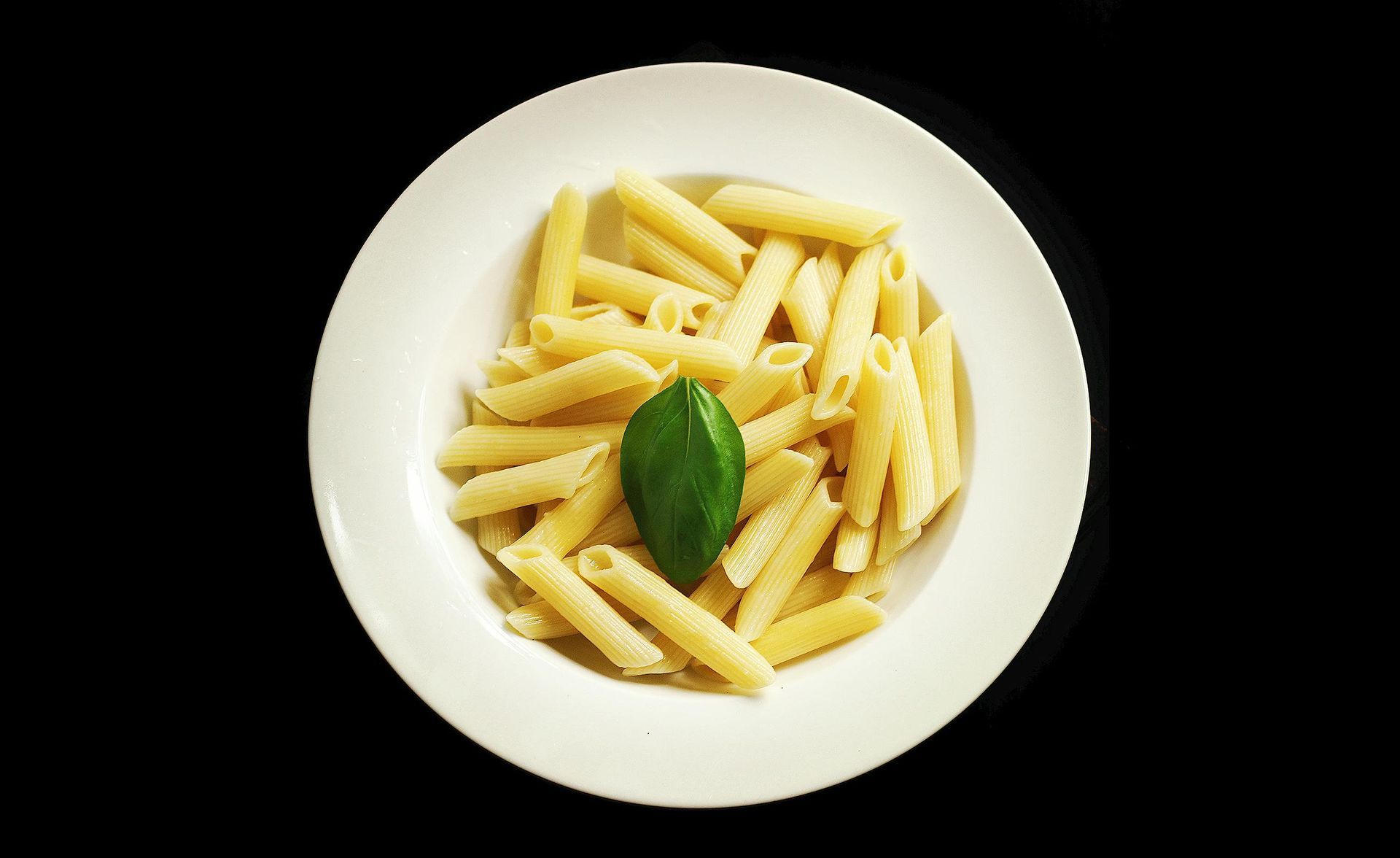A white plate topped with pasta and a green leaf on a black background.