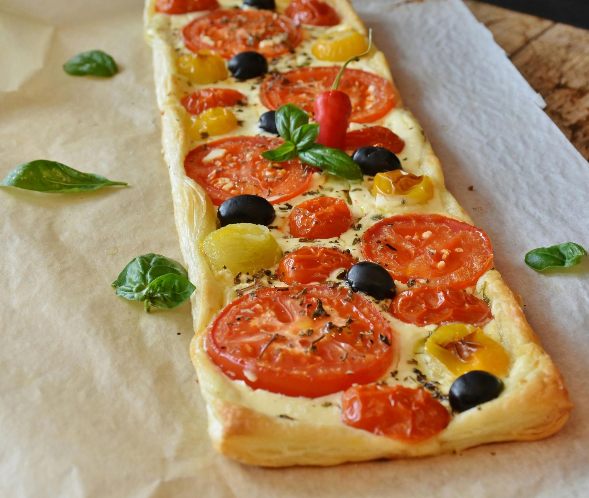 A long pizza with tomatoes and black olives on it