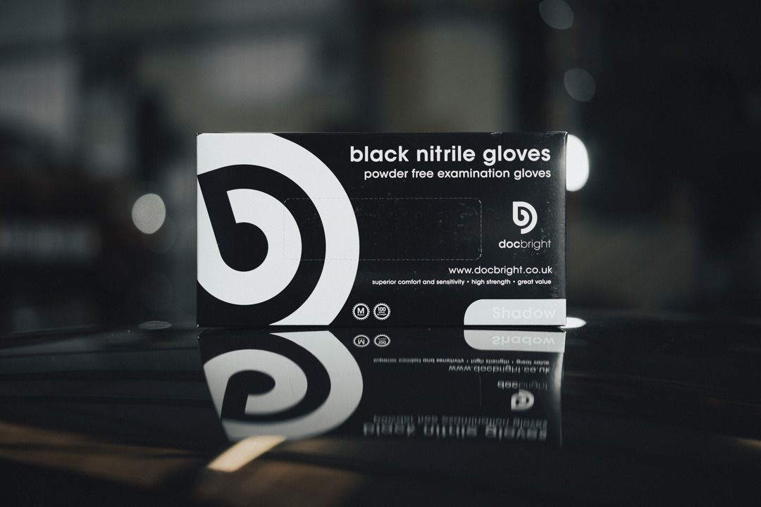 Black nitrile gloves box on a reflective surface with a spiral logo, in a dimly lit setting.
