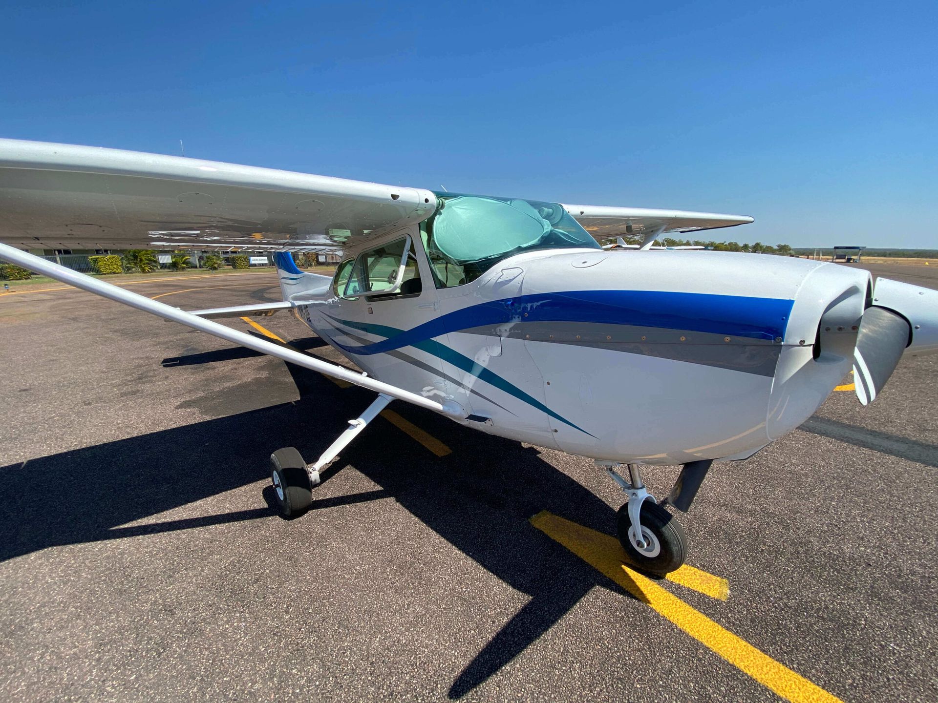 White and blue airplane parked on asphalt, sunny day.