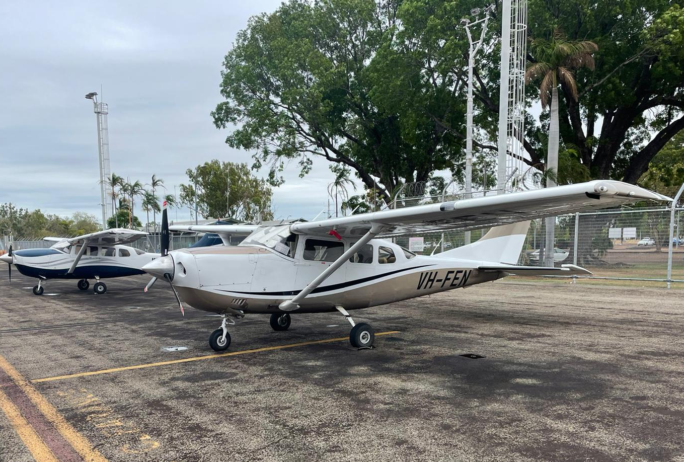 Two small airplanes parked on an asphalt surface; one white and tan, one blue.