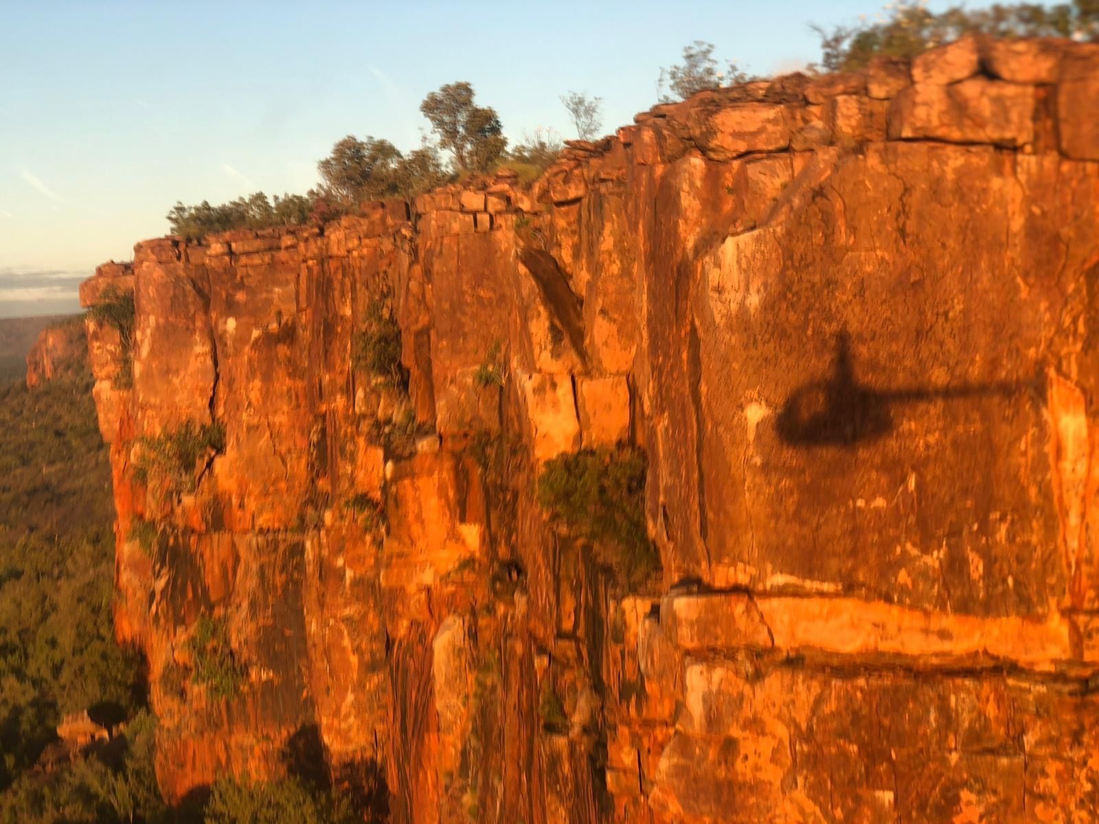 Cliff face lit by golden sunlight with a helicopter's shadow cast on the rock.