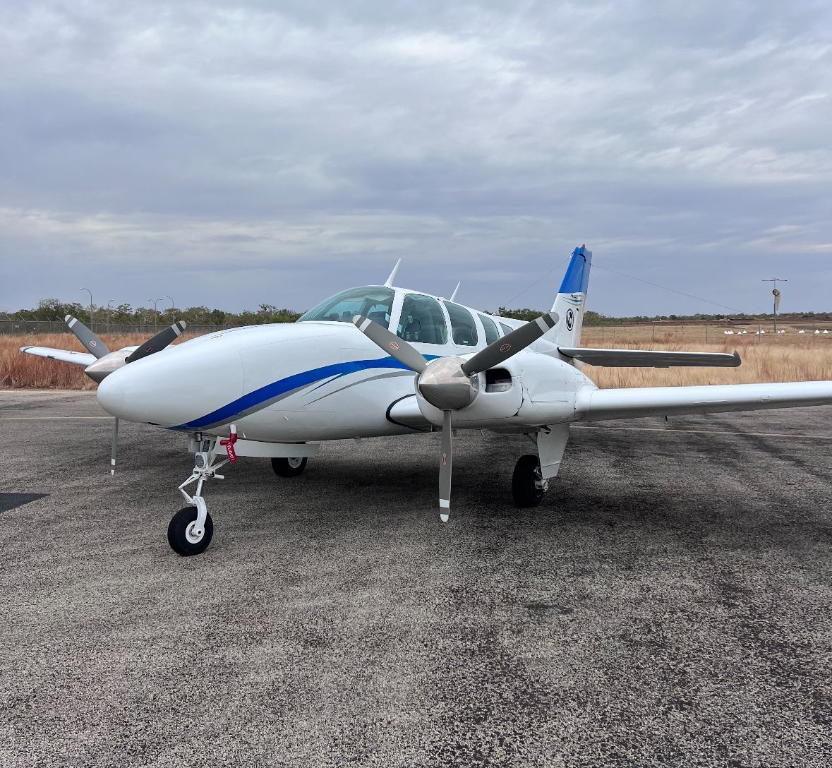 White and blue twin-engine airplane parked on a runway under a cloudy sky.