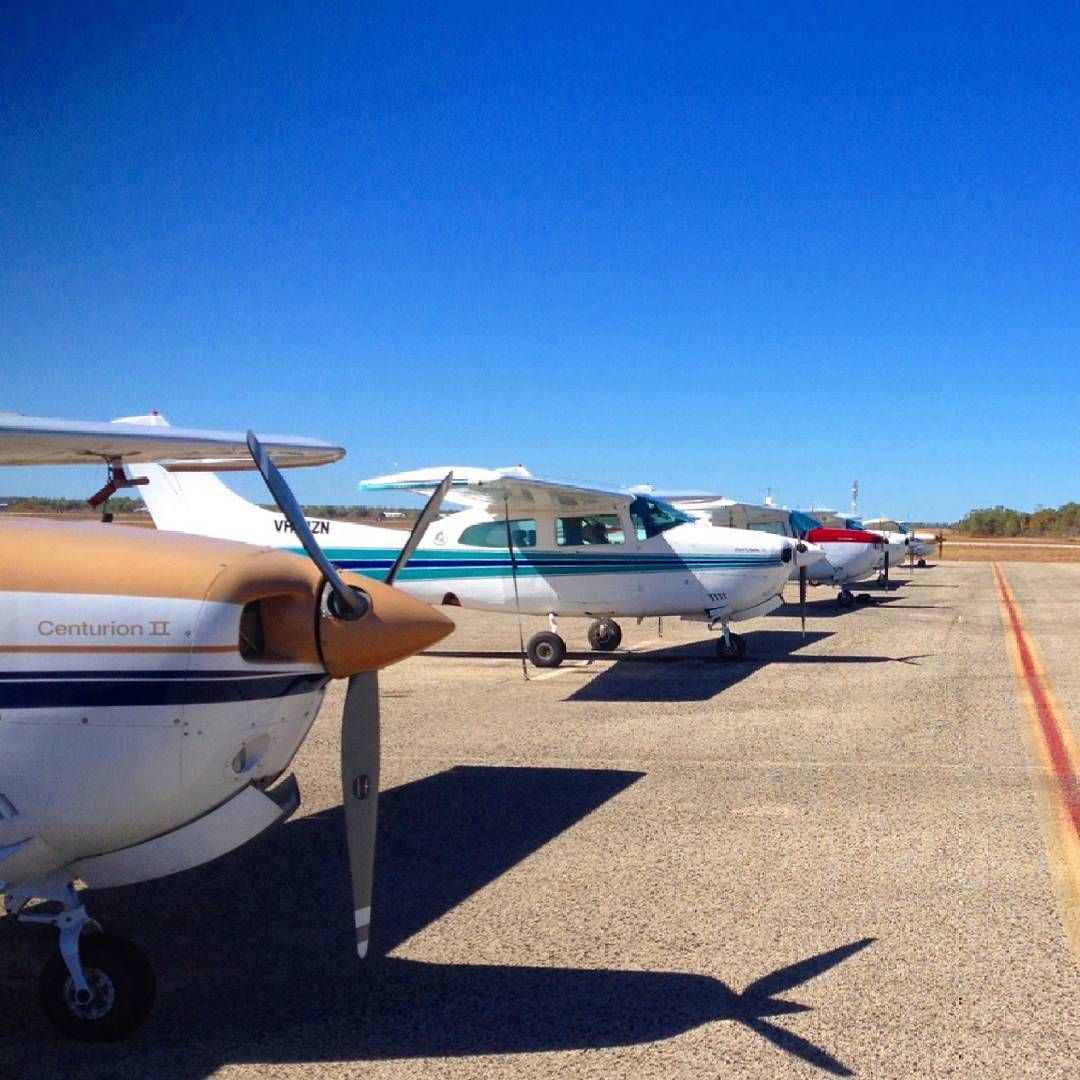 Airplanes parked on a sunny tarmac. Propeller plane in foreground; blue sky in background.