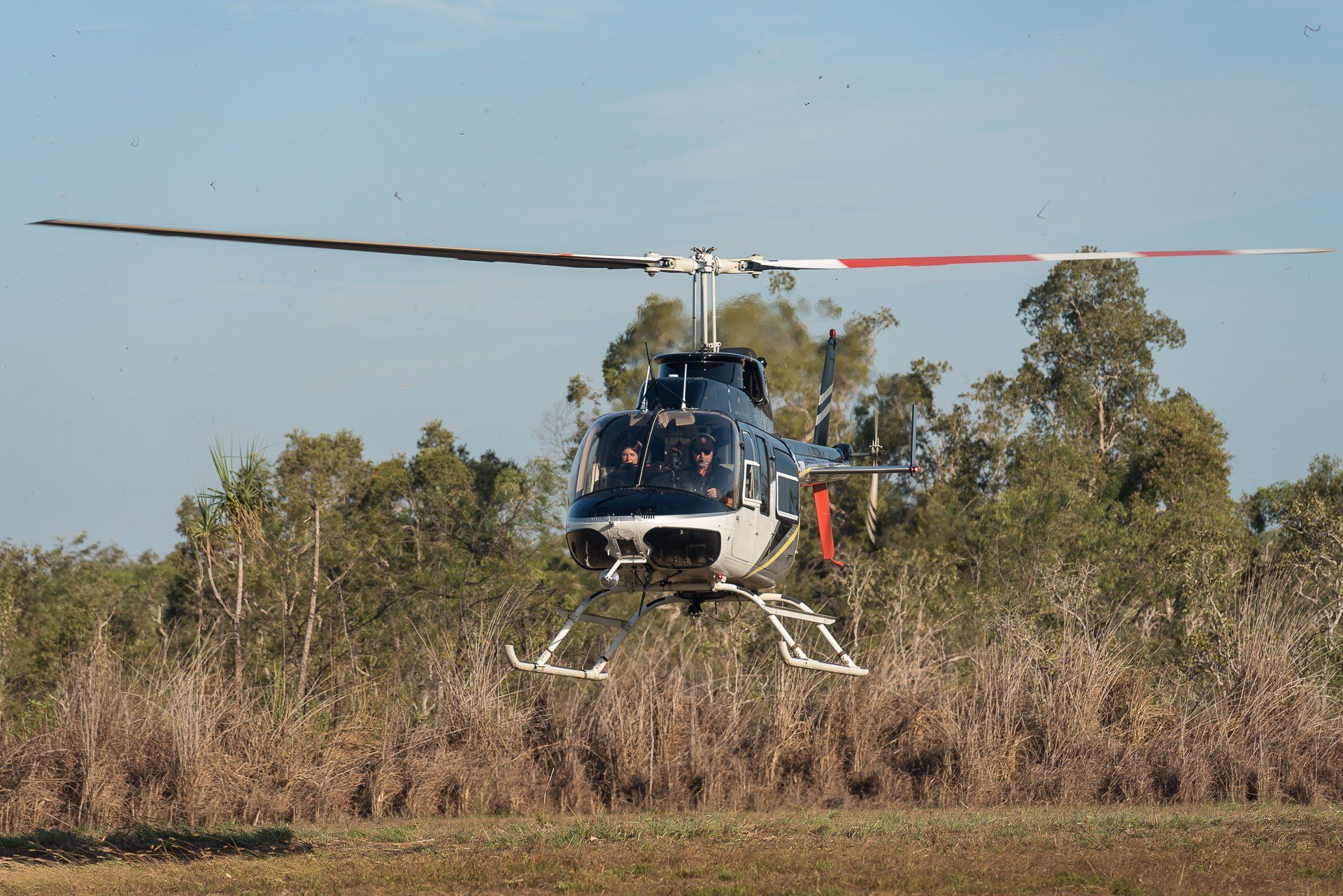 Helicopter in flight over a field with trees, blue and white with visible occupants.