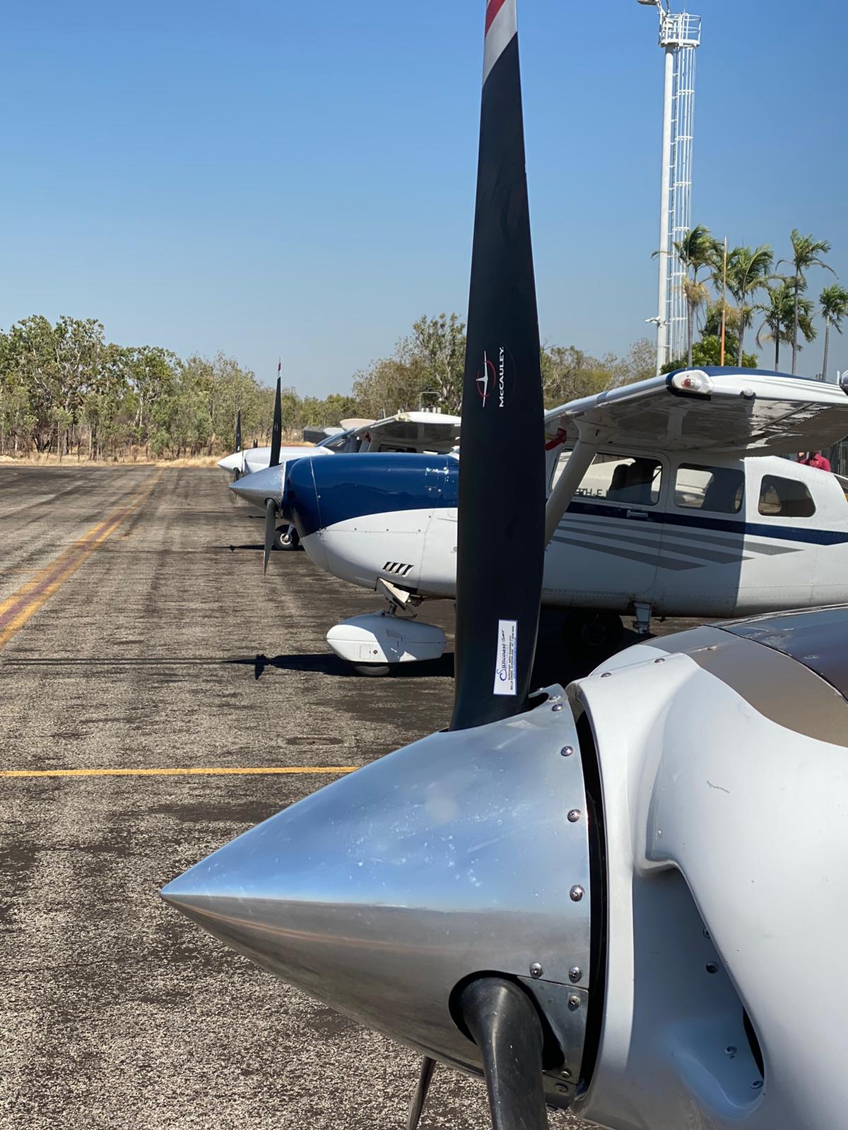 Airplane propeller close-up with other planes parked on an airfield on a sunny day.