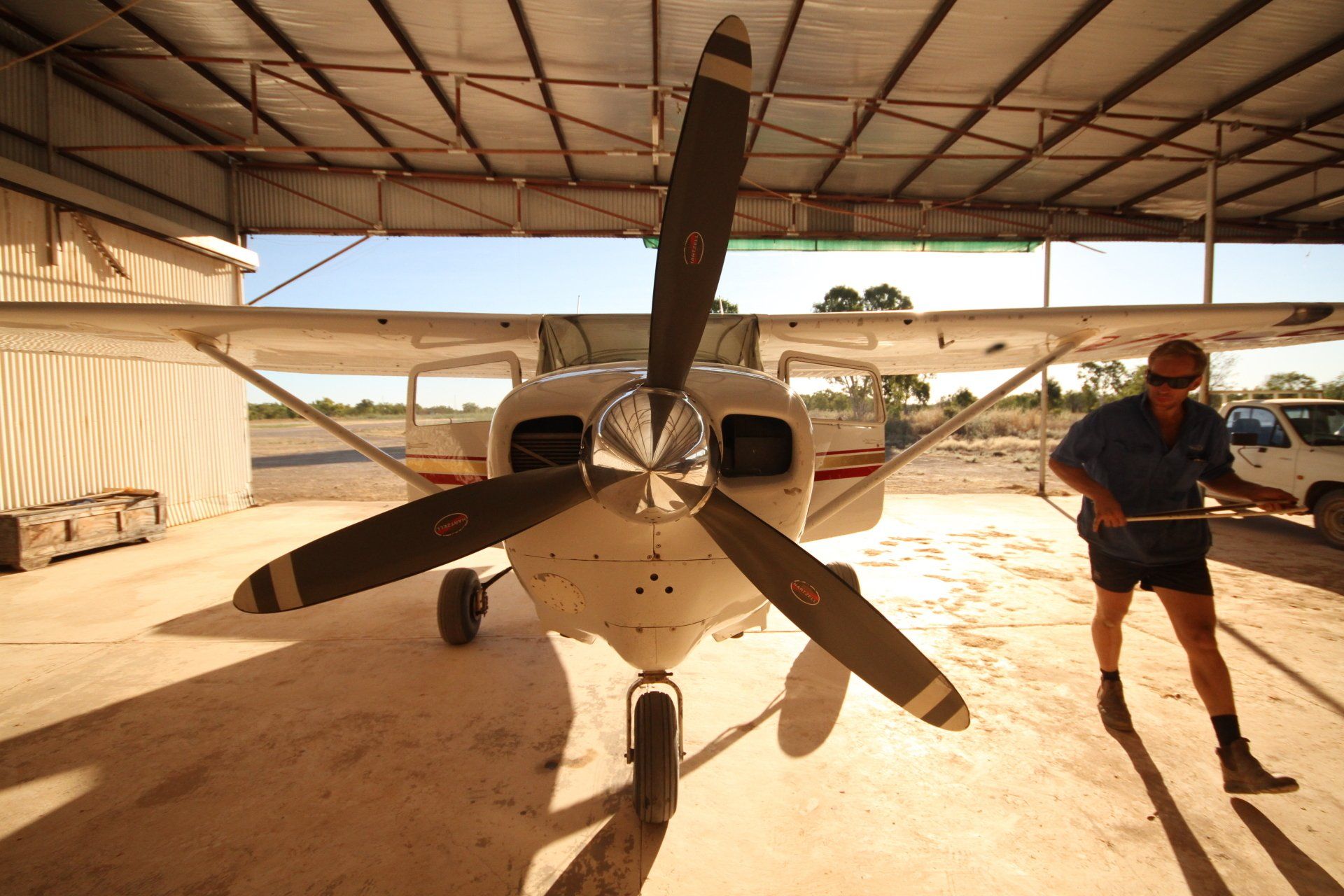 Man working on a small white airplane in a hangar; propeller in front.