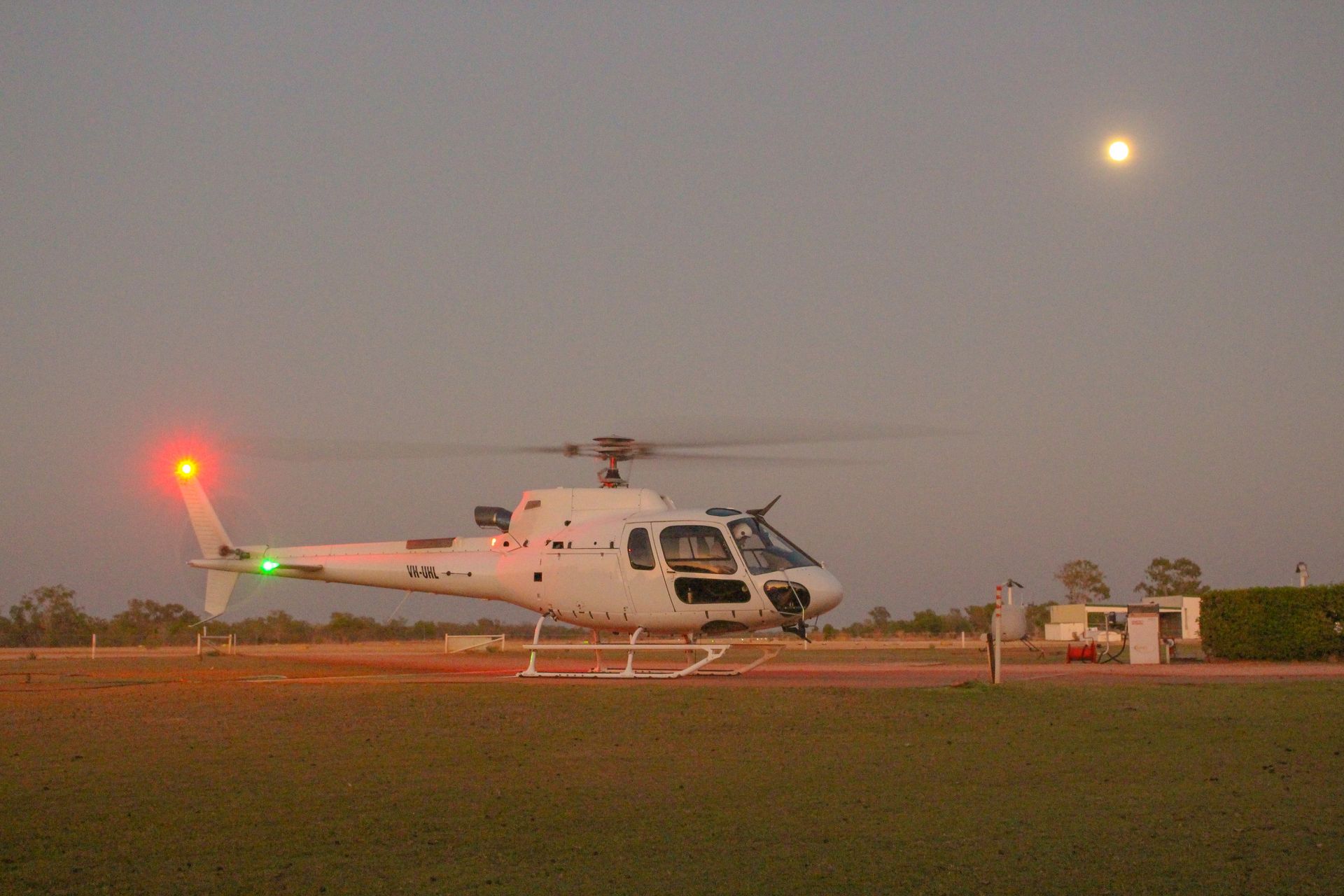 White helicopter on a grassy field at dusk with a bright moon in the background.