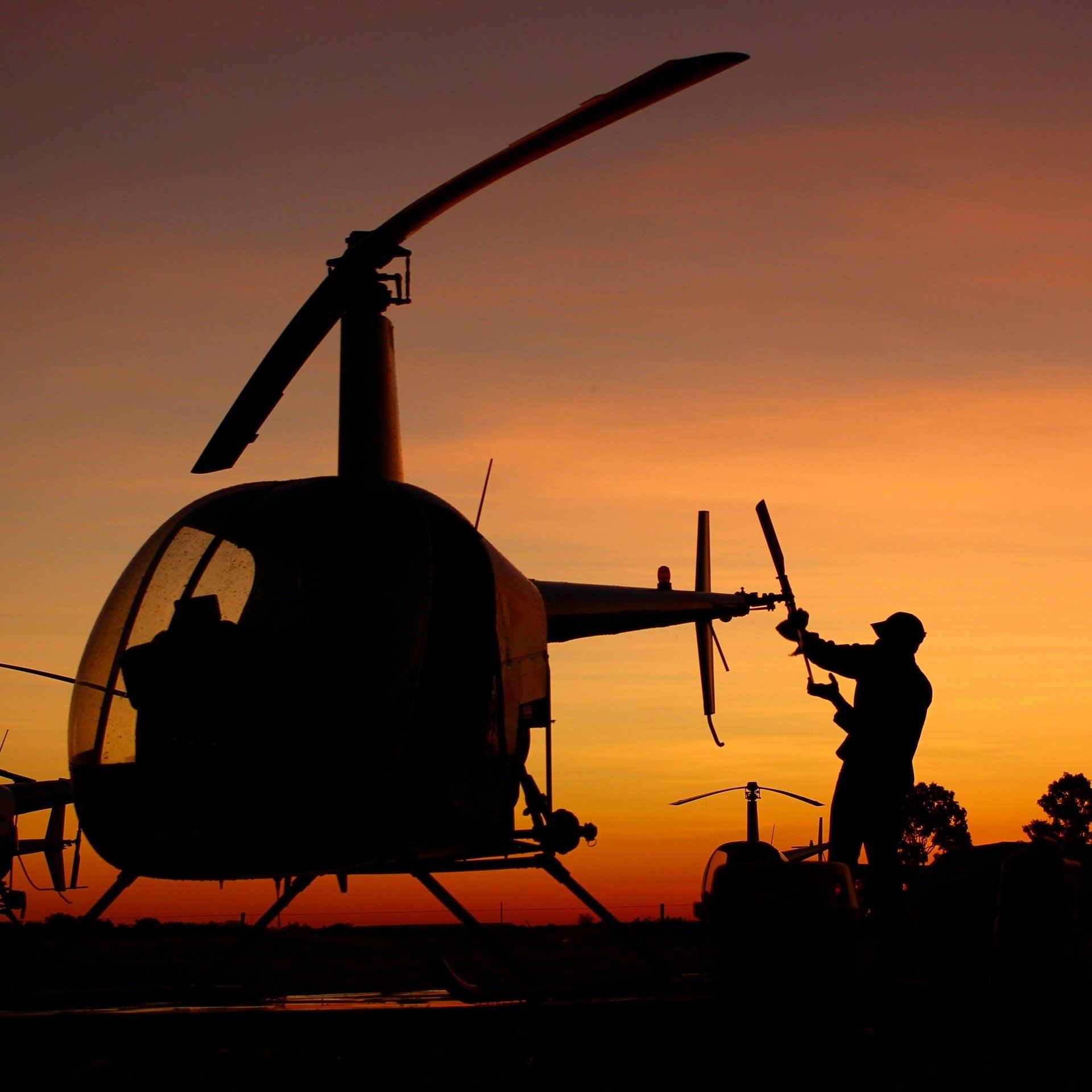 Silhouette of a helicopter and person working on it at sunset.