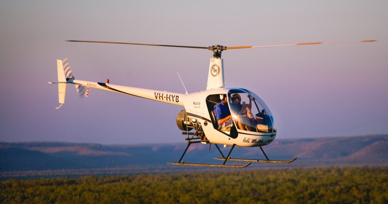 White helicopter in flight over a landscape, passengers visible, bathed in soft sunlight.