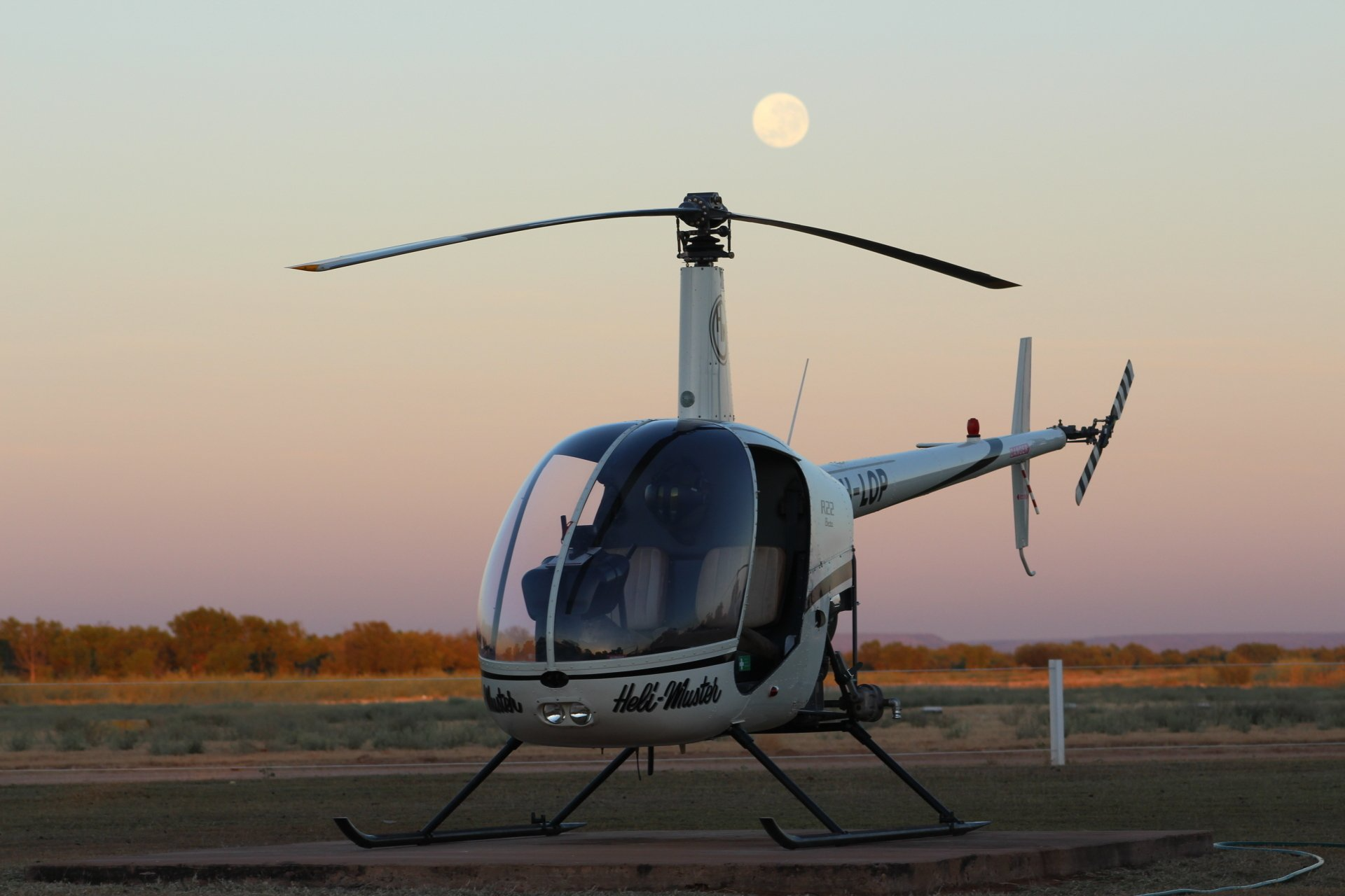 Helicopter on tarmac at dusk with full moon above.