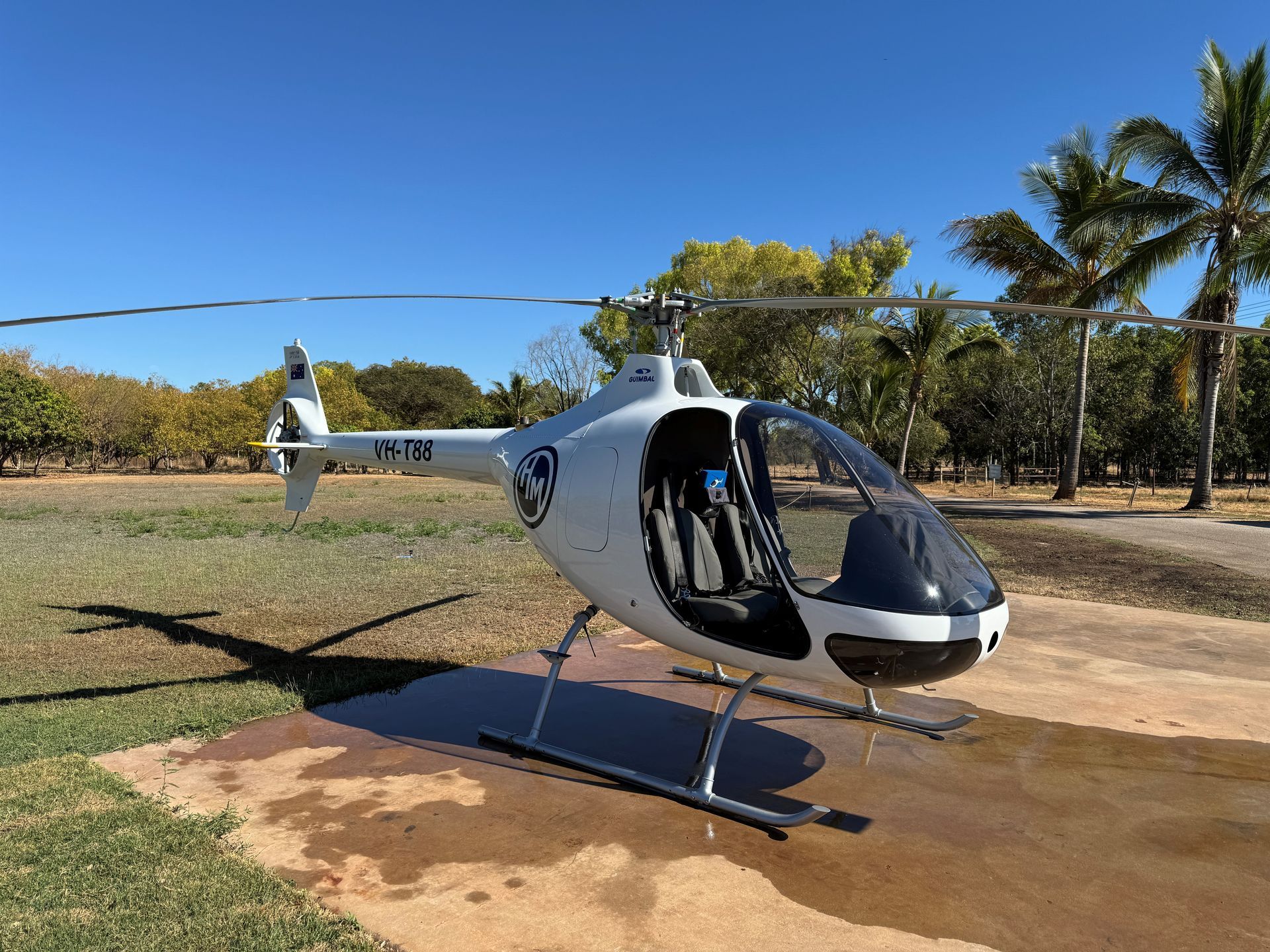 White helicopter on a concrete pad with open door, under blue sky, palm trees in background.