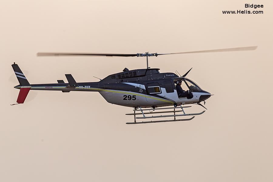 Black and white helicopter in flight with a red tail fin and landing skids, against a muted sky.