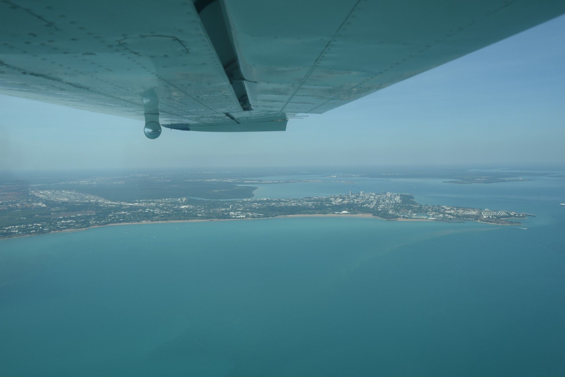 Small plane flies over a vast green landscape under a partly cloudy sky.