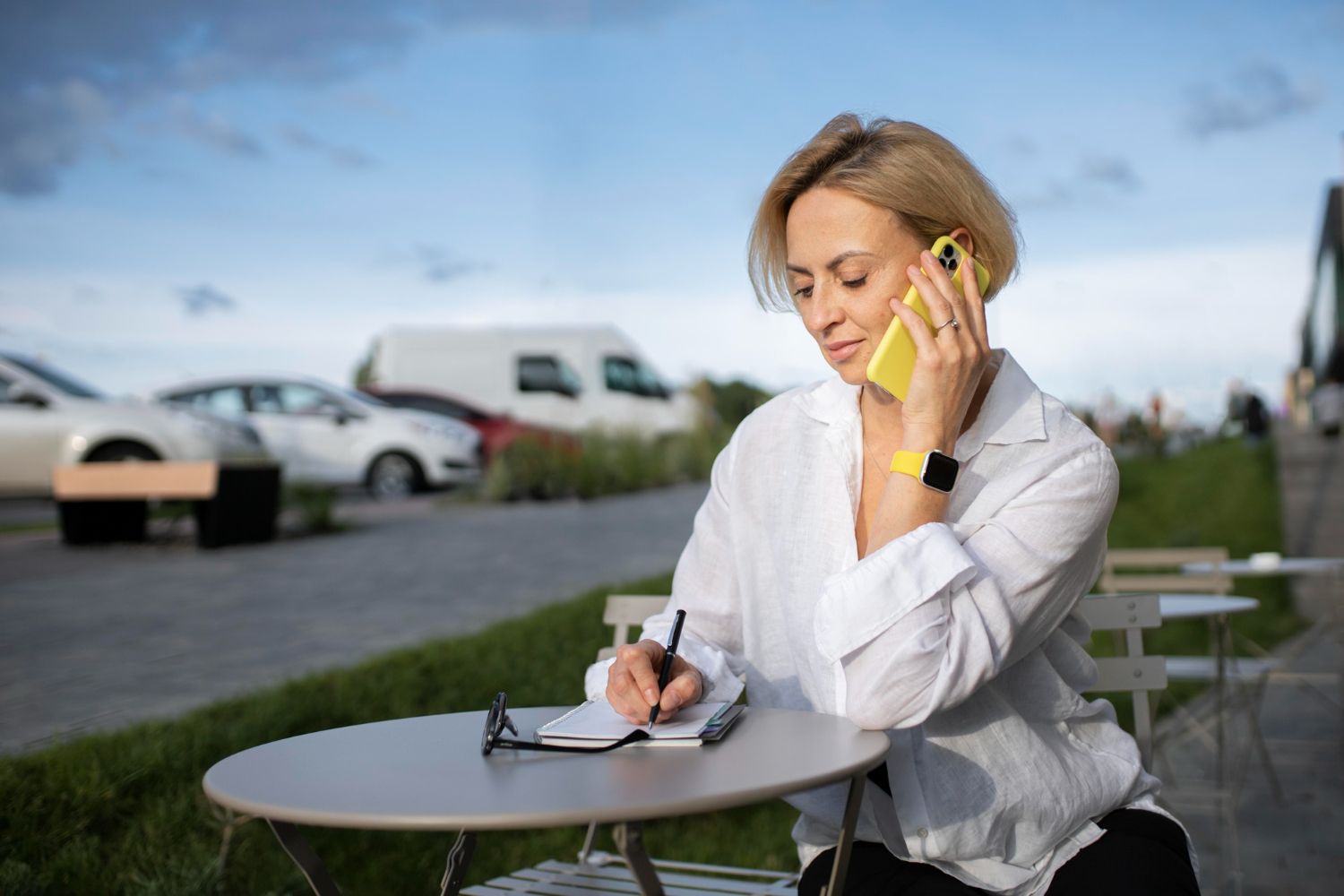 Mujer con gafas de sol, leyendo un mapa en una estación de tren, con una maleta, una mochila y un sombrero.