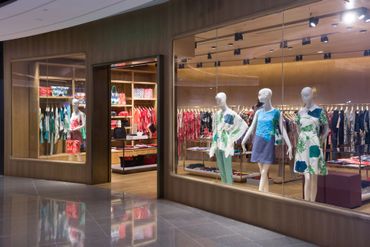 L'ingresso di un negozio di abbigliamento con manichini che espongono abiti a fantasia in ampie vetrine.