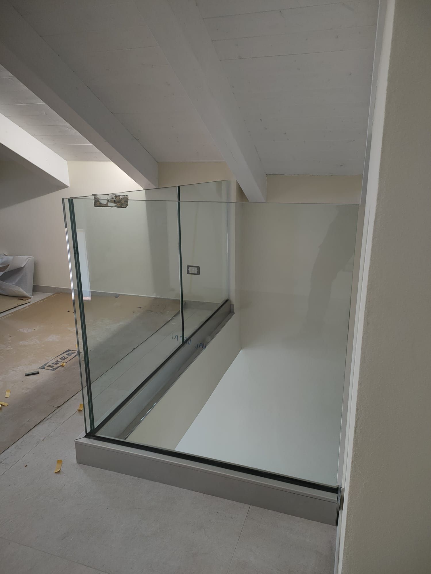 Box doccia in vetro con accessori cromati, installato su una base bianca rialzata in una stanza in fase di ristrutturazione.