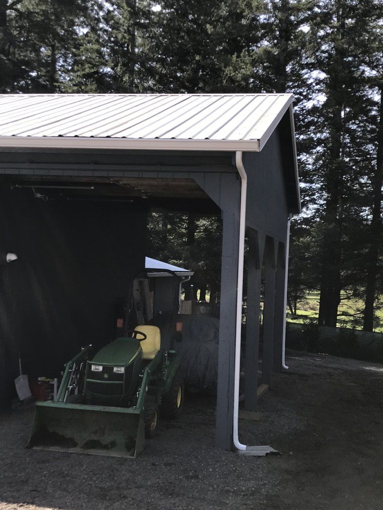 Gray shed with white metal roof, gutters, and a green tractor parked inside.