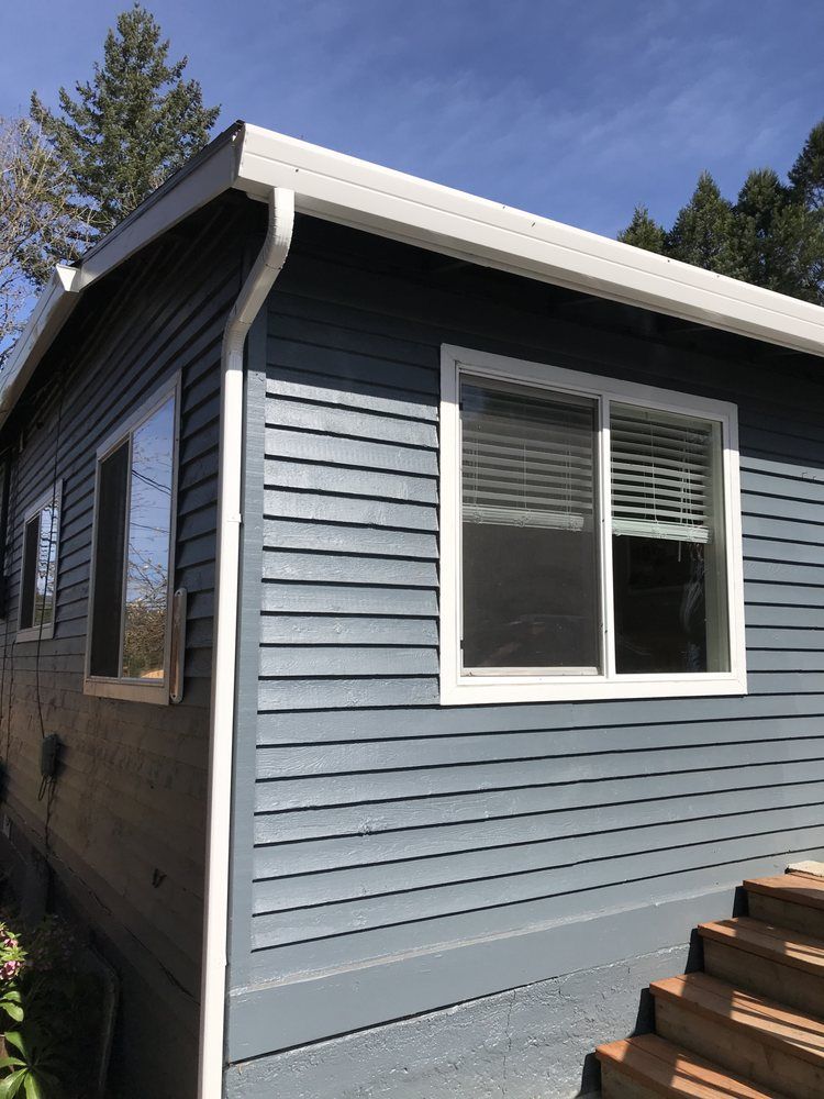 Blue-gray house with white trim, windows, and gutter against a blue sky, wooden steps in foreground.
