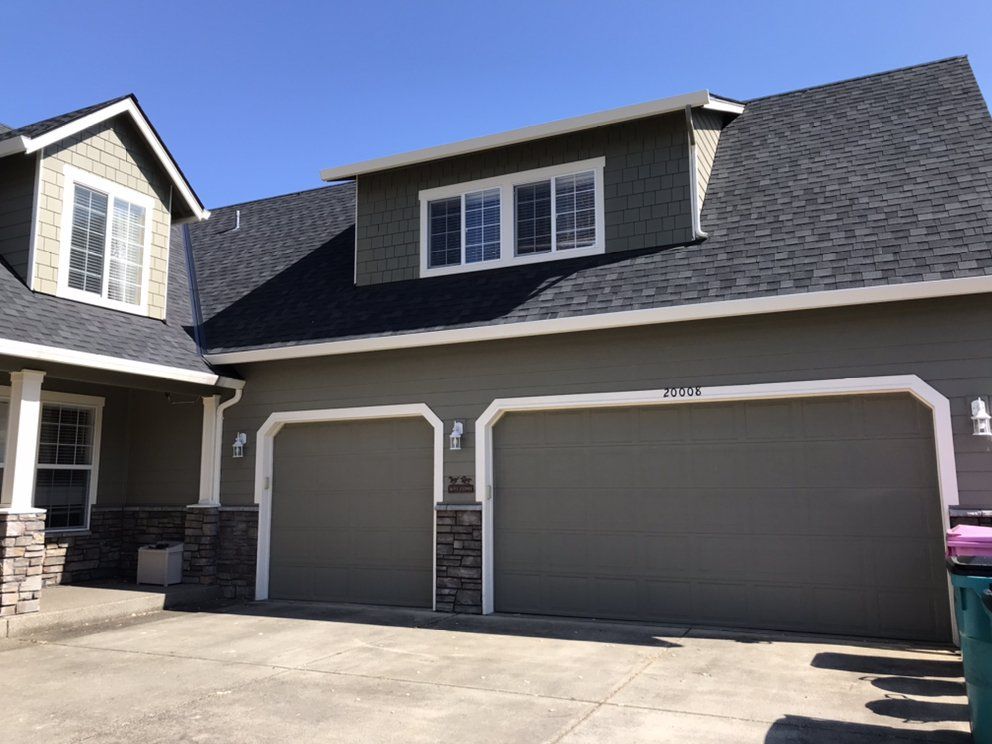 Green house with gray garage doors, dormers, and dark gray roof.
