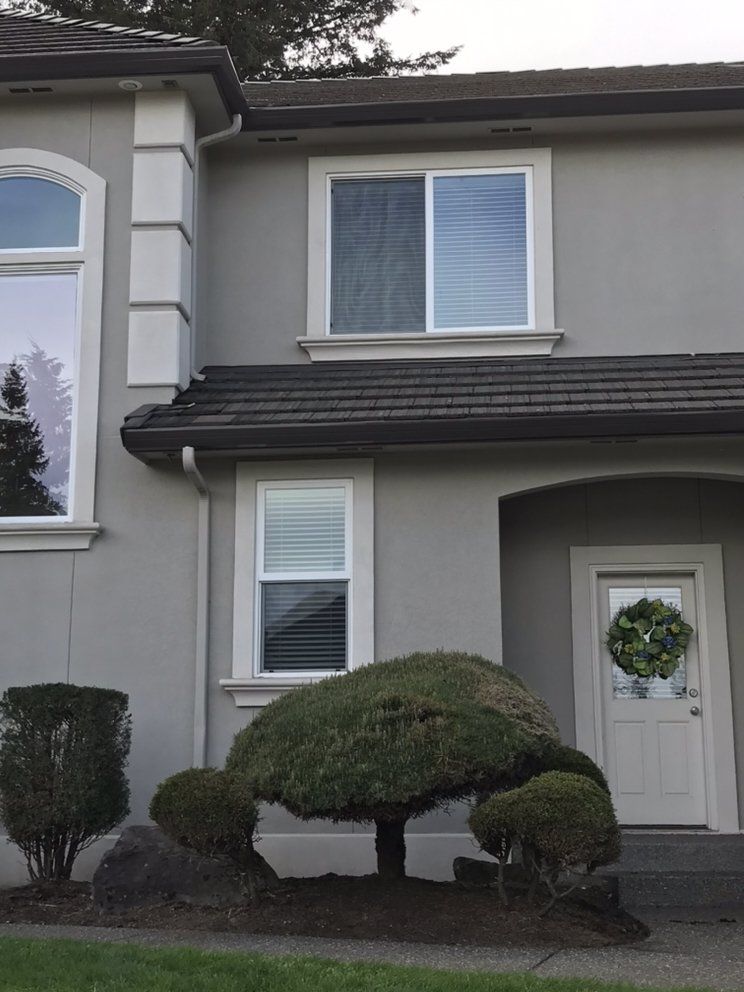Gray house exterior with white trim, windows, and a wreath on the door. Bush in front.