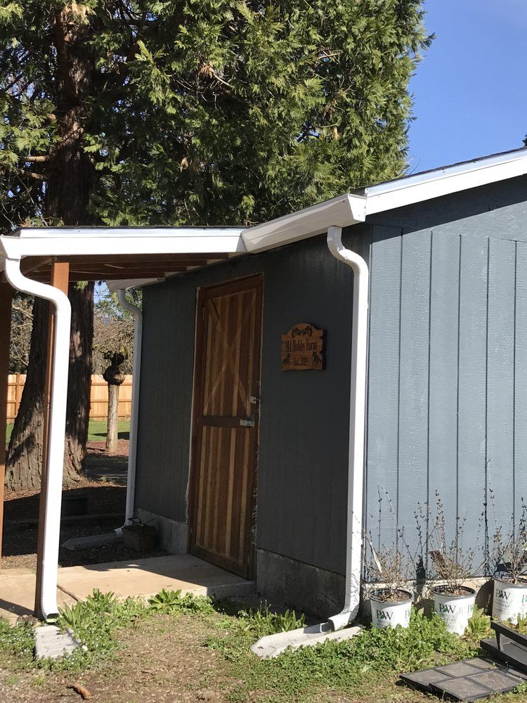 Blue shed with white trim, brown door, and gutters. Wooden sign above the door.