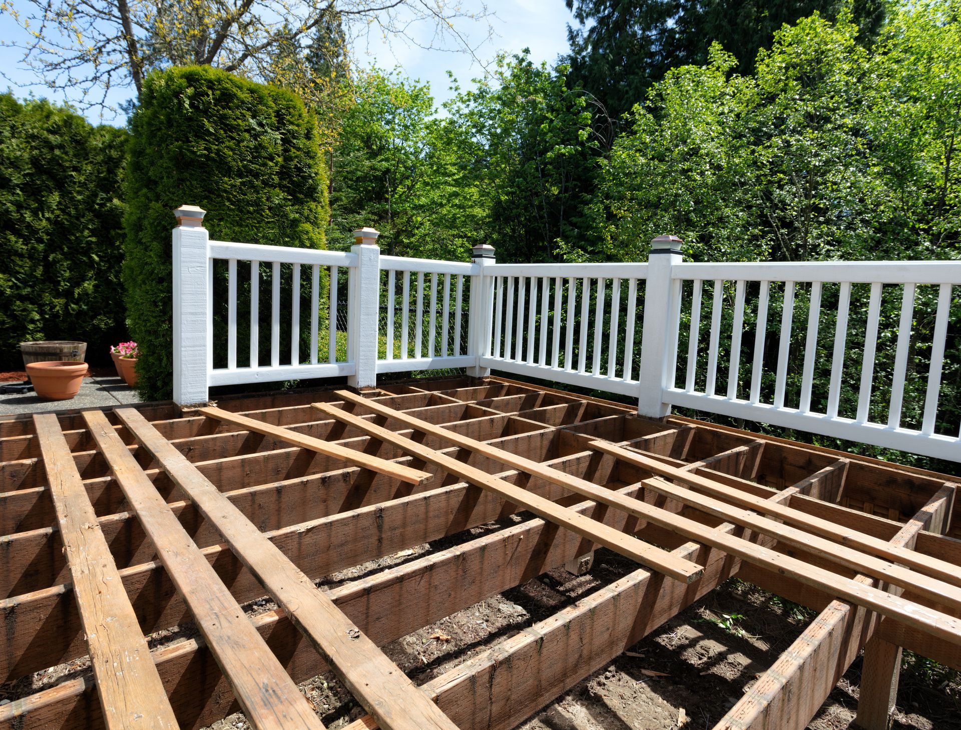 Deck framing under construction beside a white railing and green garden