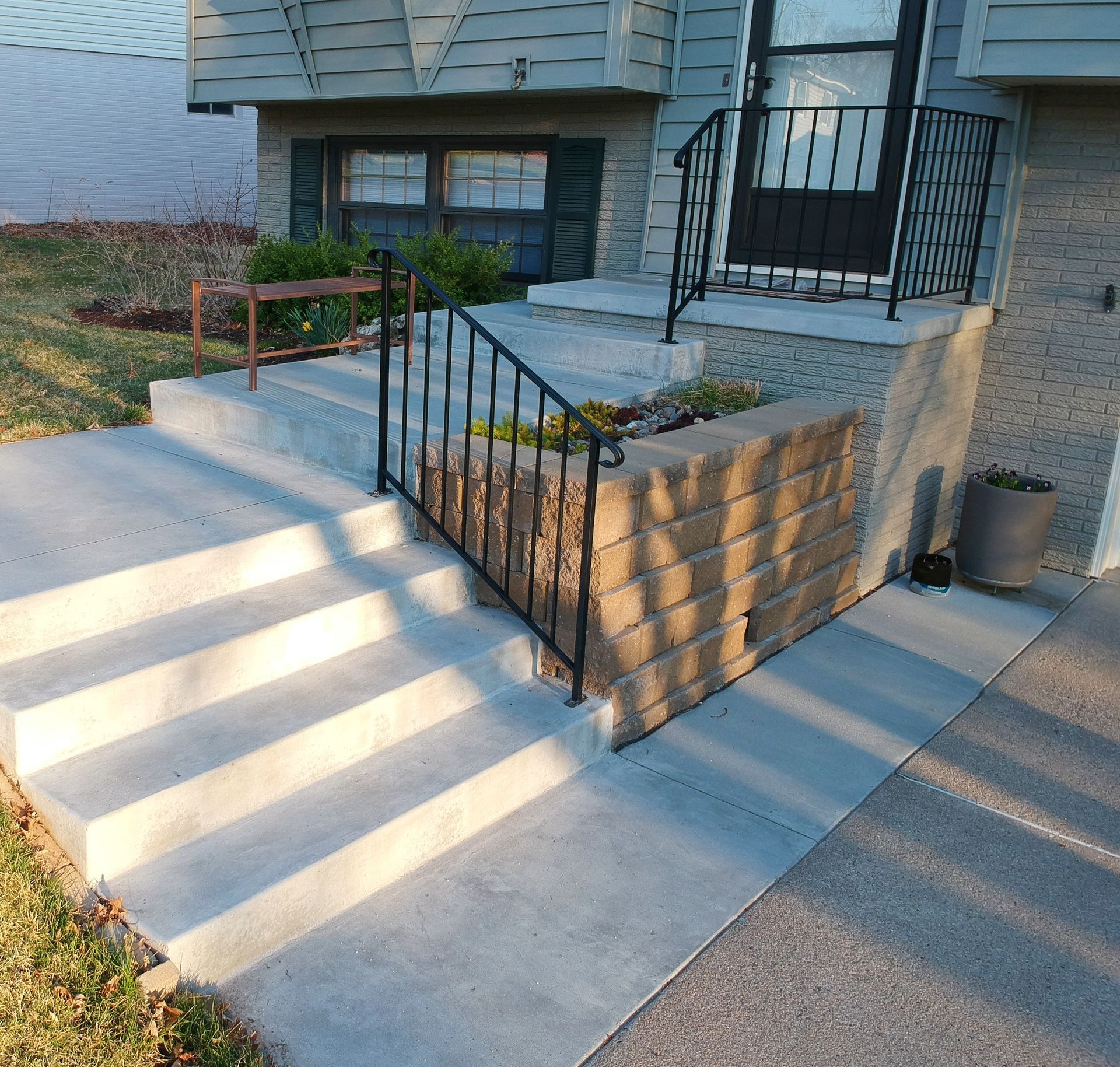 Concrete porch ramp with black metal railings and stairs beside a house.