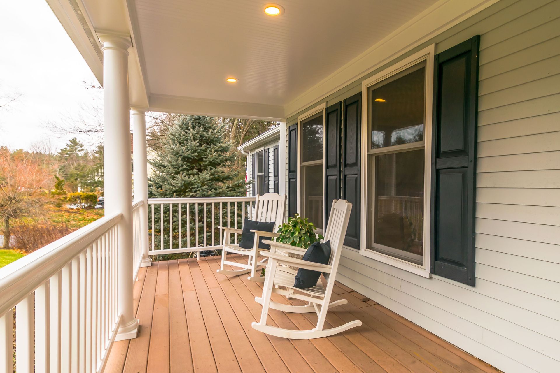 Covered front porch with white rocking chair, wooden floor, and railing on a house exterior.