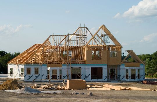 Wood-framed houses under construction along a paved street on a sunny day
