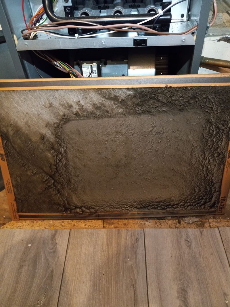 A dirty air filter is sitting on top of a wooden floor next to a stove