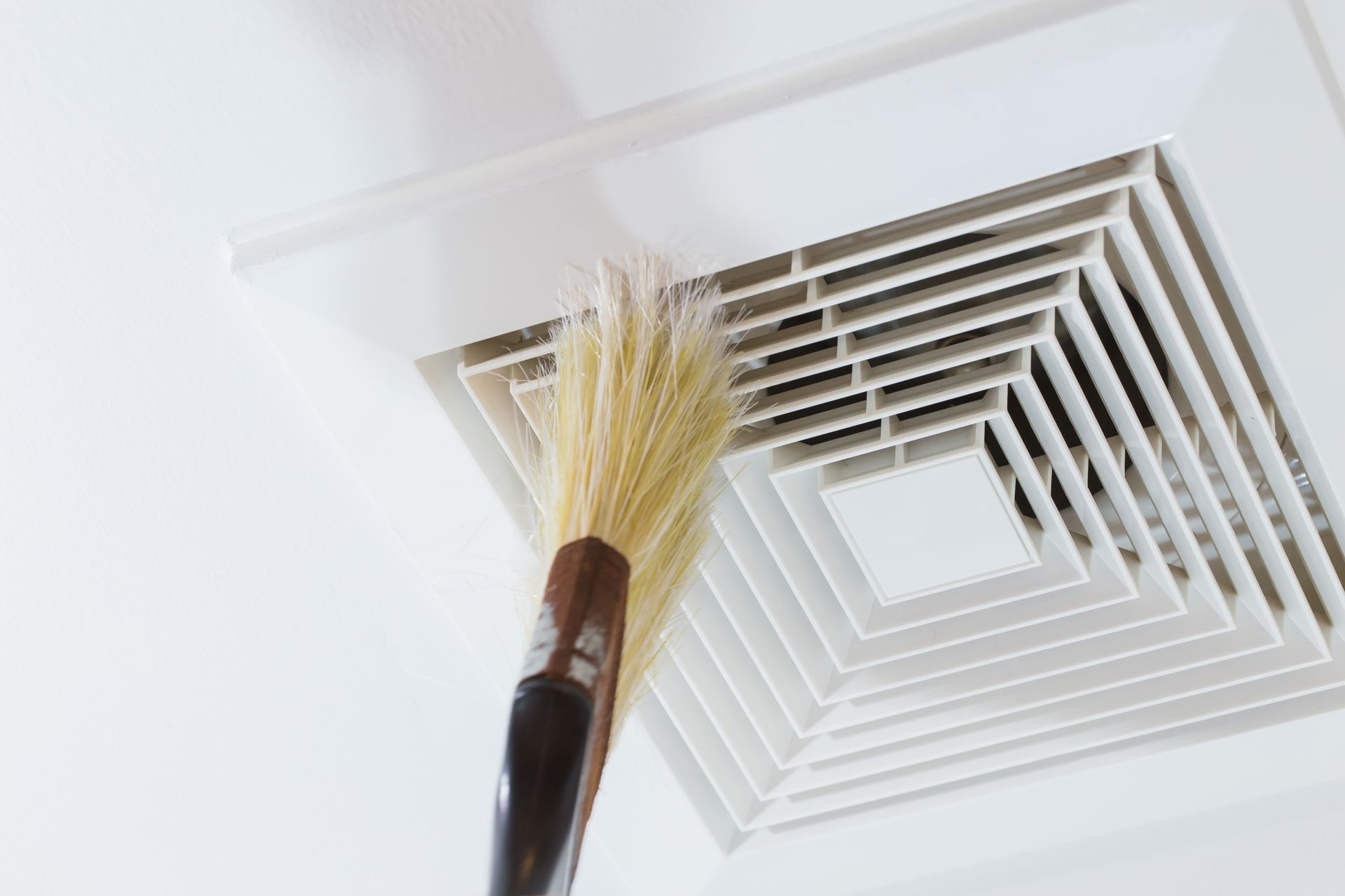 A person is cleaning a ceiling vent with a broom.