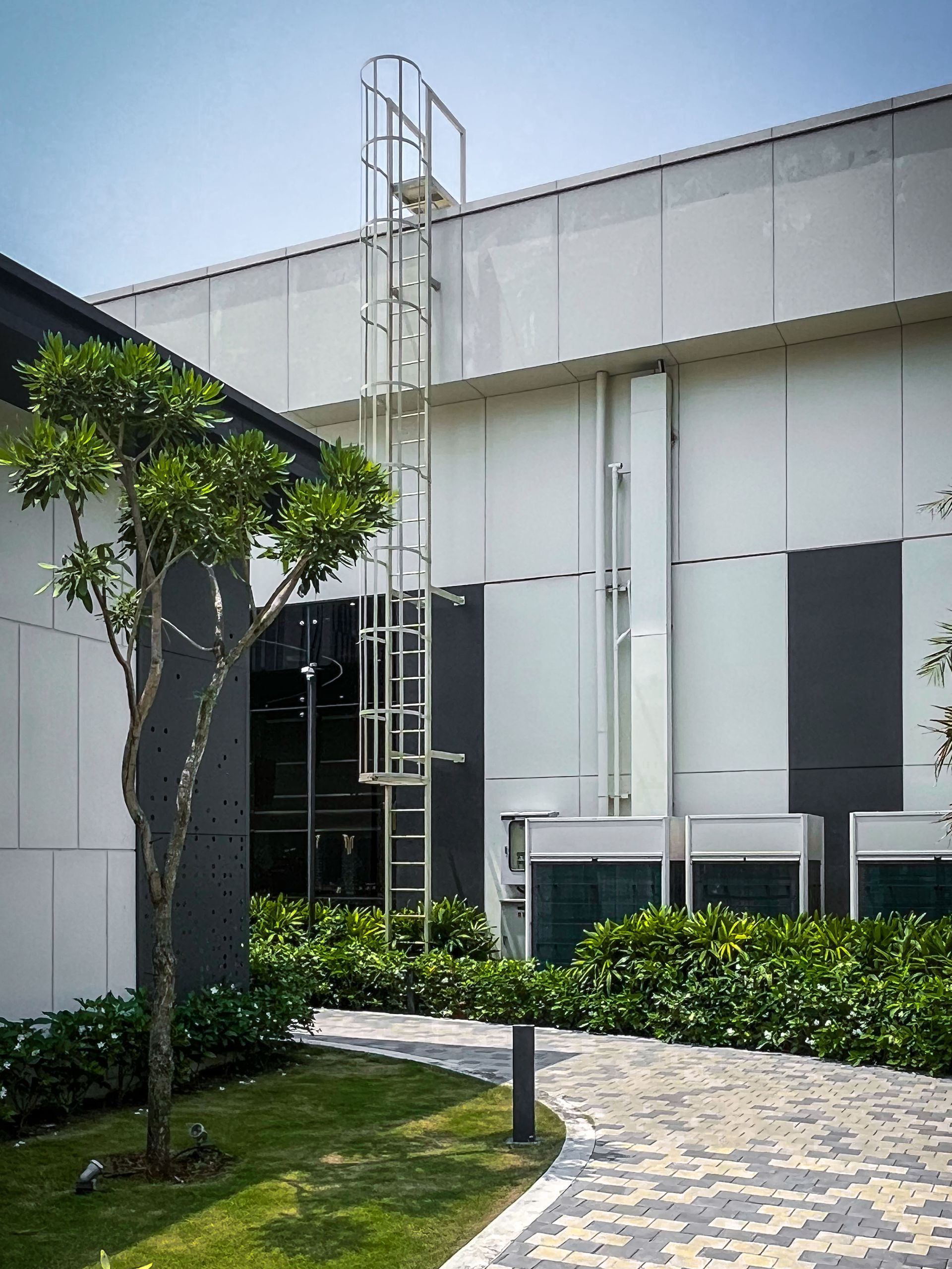 Modern white building exterior with a ladder tower, lawn, and paved walkway