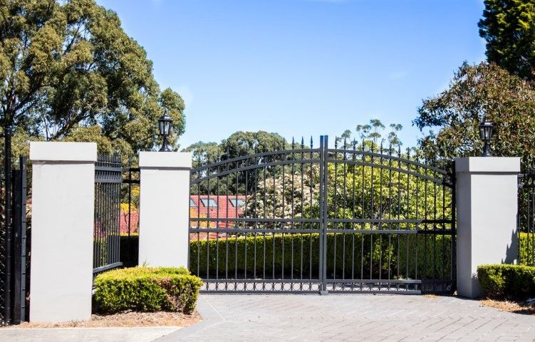 The Cheval property features black metal driveway entrance gates set in a brick white fence