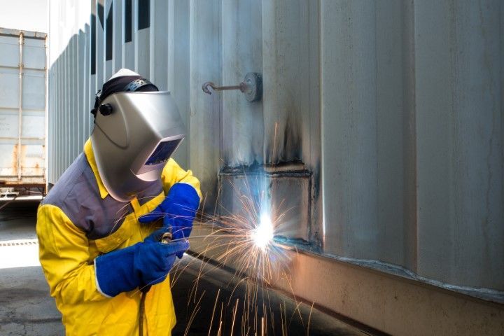 worker repairing container structure with welding steel in an industrial setting