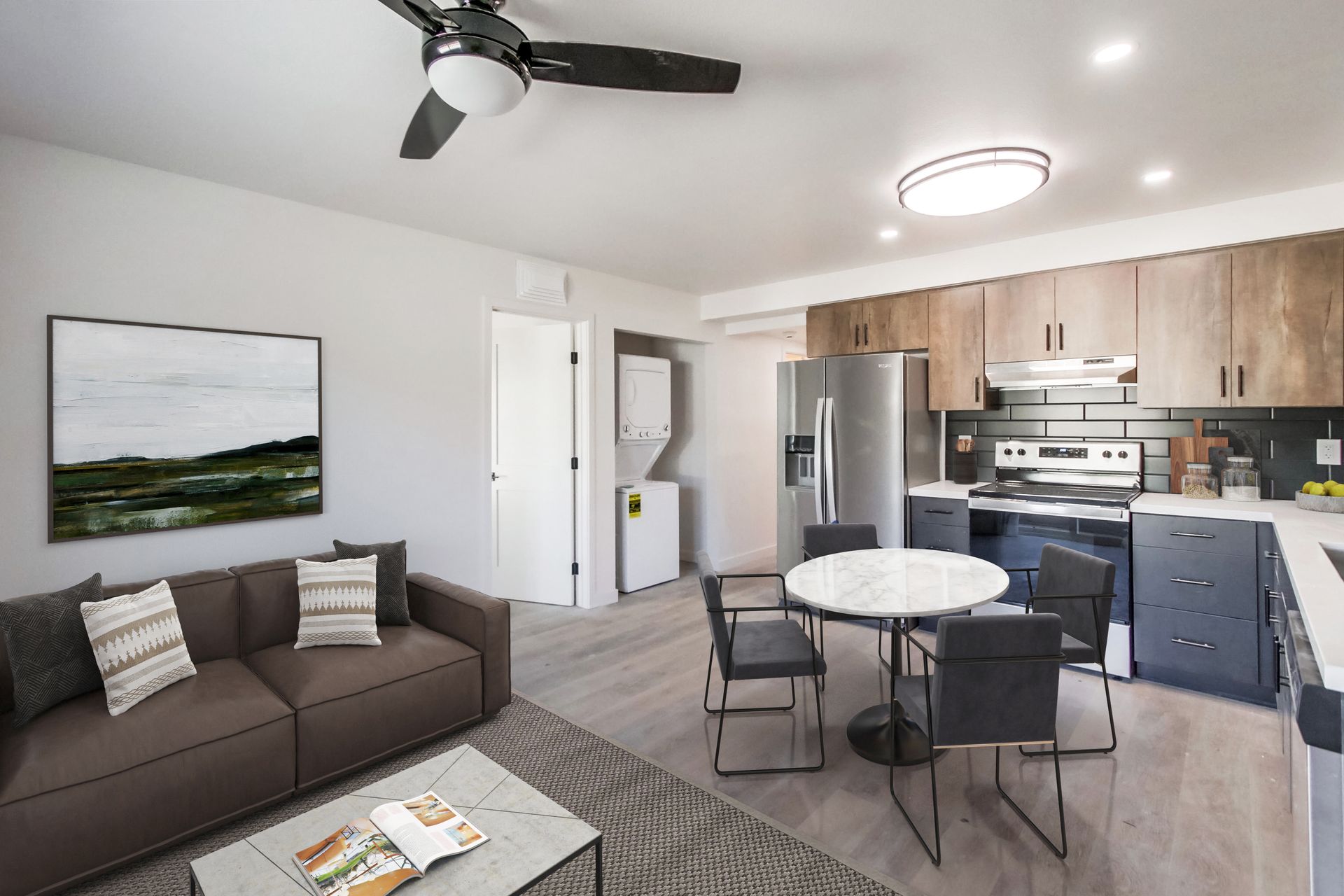 Modern open-plan studio apartment with a brown sofa, small dining table, and kitchen with dark grey and wood cabinetry.