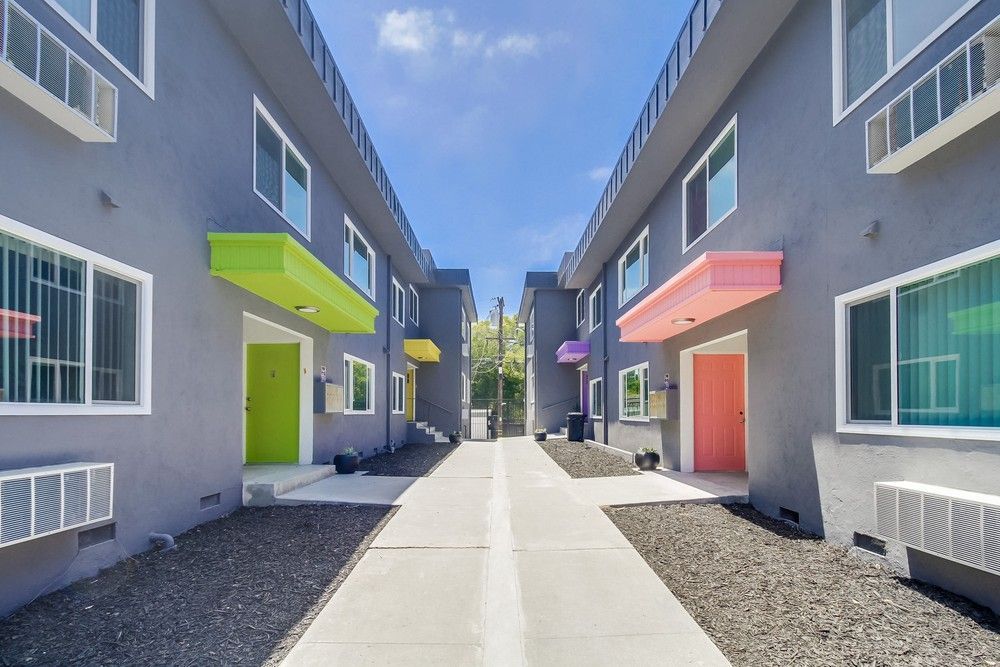A walkway between two grey apartment buildings featuring bright green and pink awnings and matching front doors.