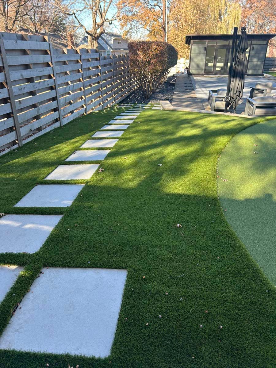 A backyard with a wooden fence and green artificial turf lawn.