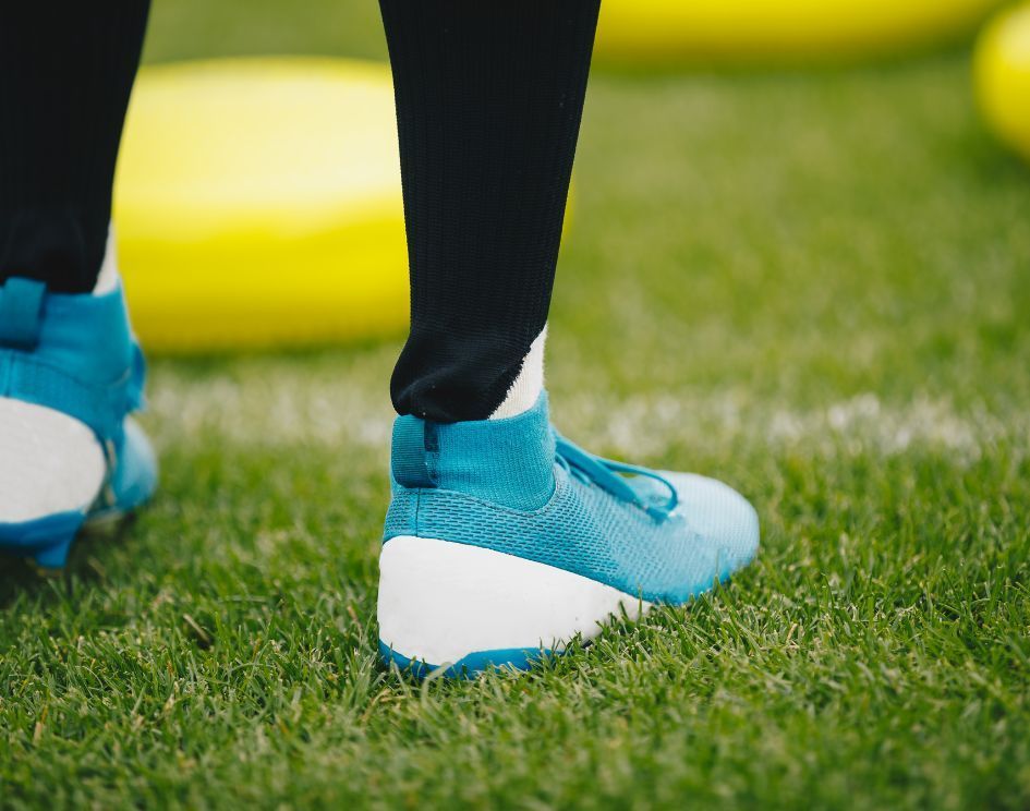 A person wearing blue and white soccer cleats is standing on a soccer field.