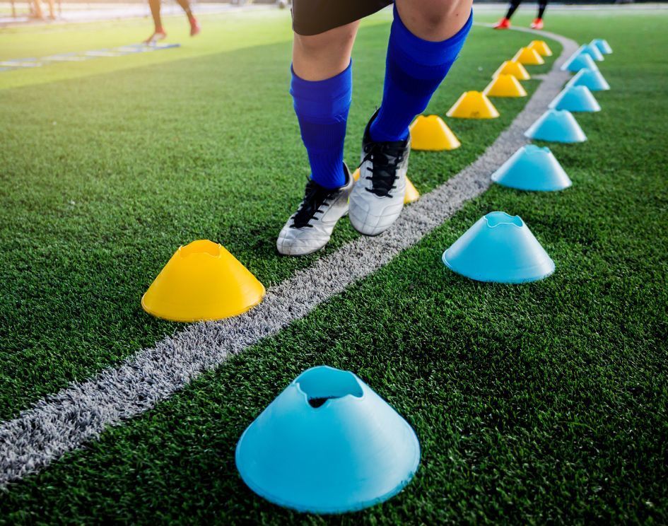 A soccer player is jumping over cones on a field.