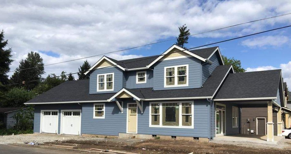 Blue two-story house with white trim, two-car garage, and covered entryway. Partly cloudy sky.