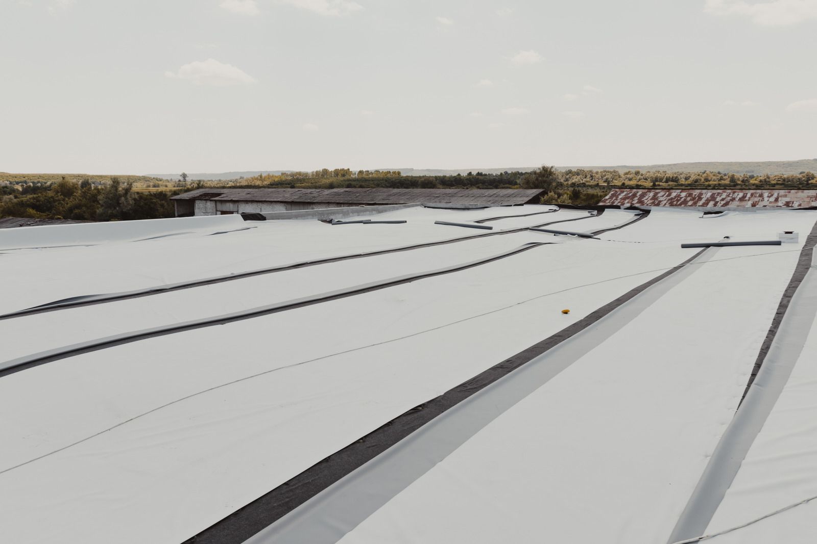 Flat white roof with black seams under a partly cloudy sky.