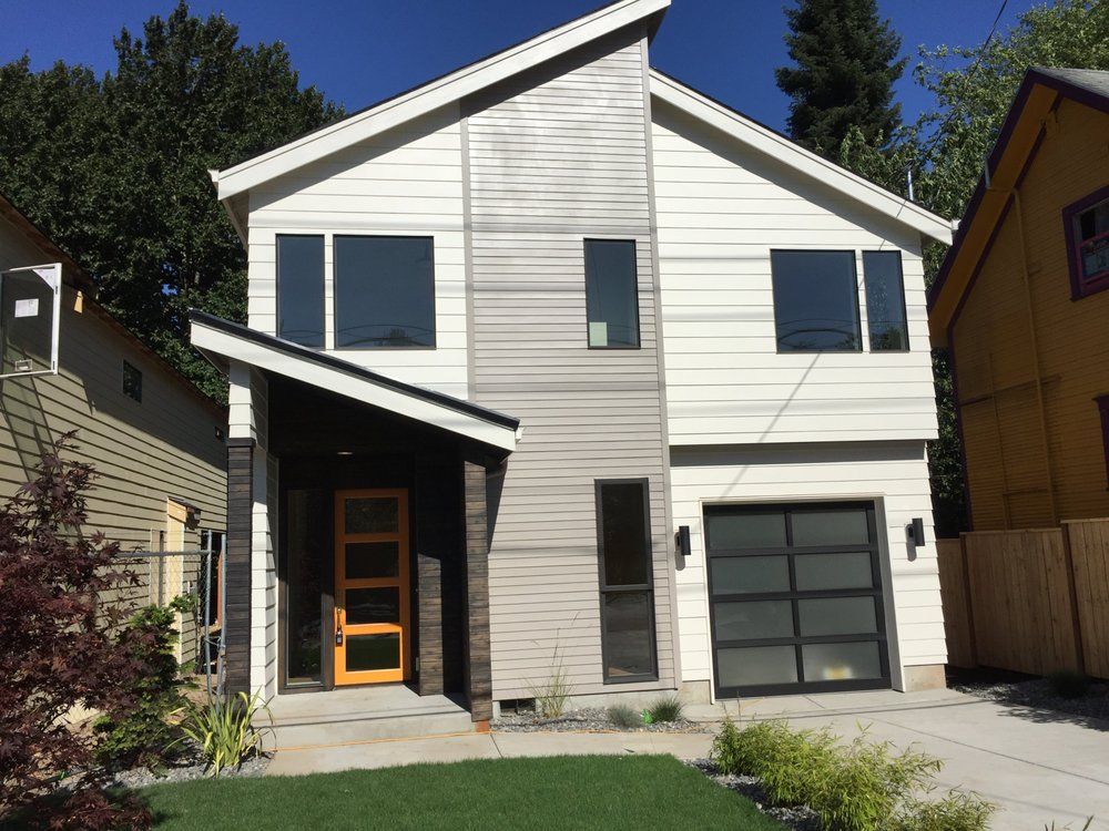 Modern two-story house with gray and white siding, a black garage door, and a yellow front door.